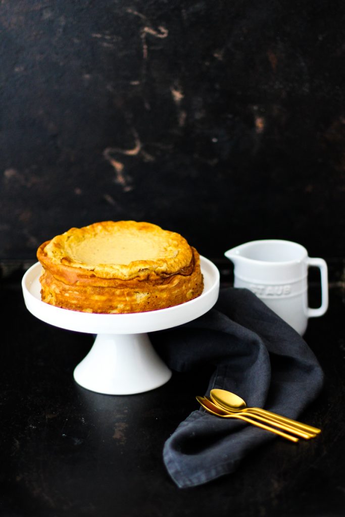 Käsekuchen auf einer weißen Tortenplatte mit goldenen Löffeln und einer weißen kleinen Milchkanne