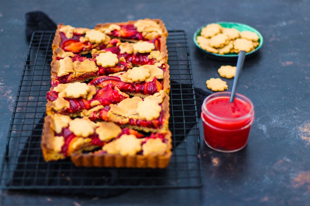 Mürbeteig Pflaumenkuchen mit Mürbeteigblumen, aufgeschnitten, auf einem schwarzen Gitter 