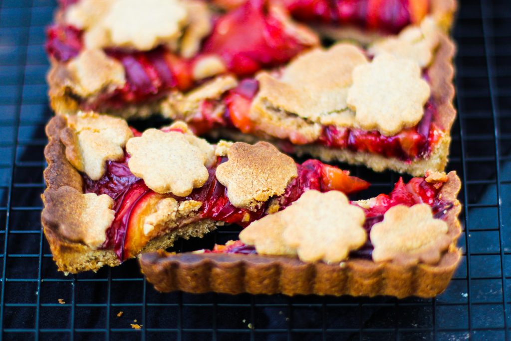 Mürbeteig Pflaumenkuchen mit Mürbeteigblumen auf einem schwarzen Gitter aus der Nähe 