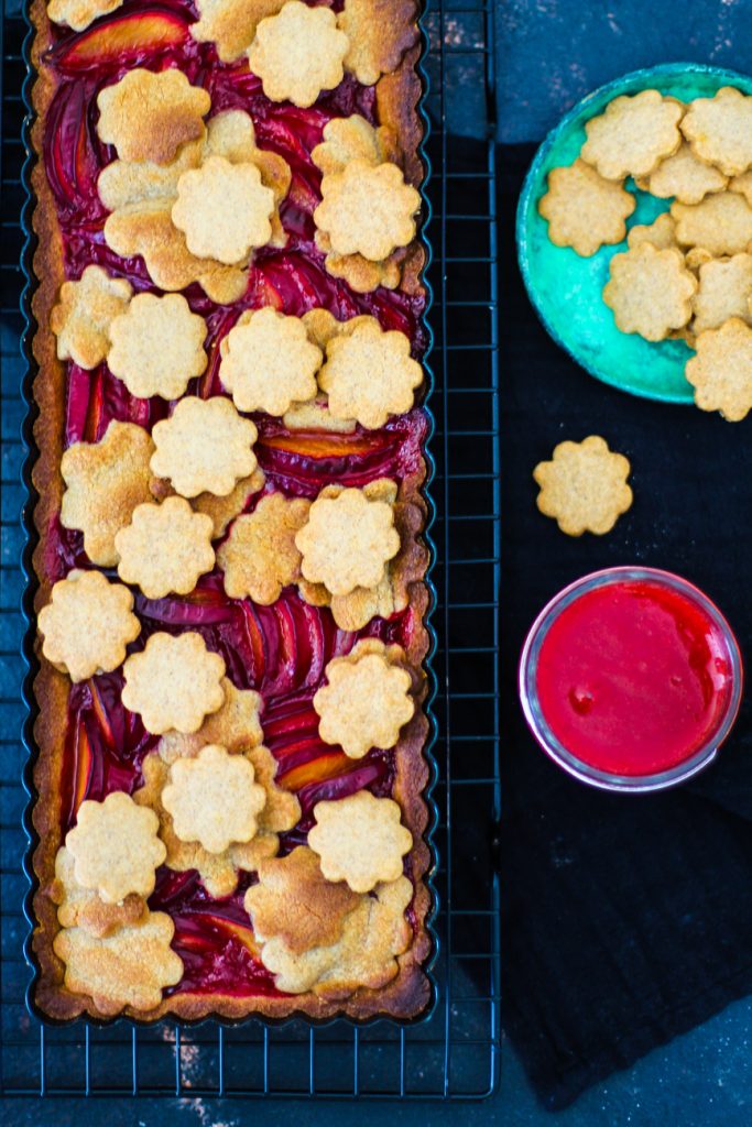 Pflaumenkuchen auf einem Gitter, der Kuchen ist mit Blumenkeksen dekoriert