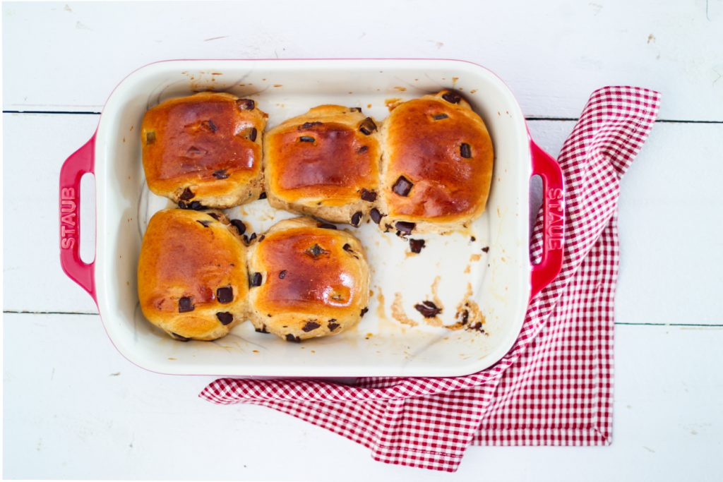 Schokoladenbrötchen aus Hefeteig in einem roten Bräter. Daneben ein rot-weiß kariertes Tuch