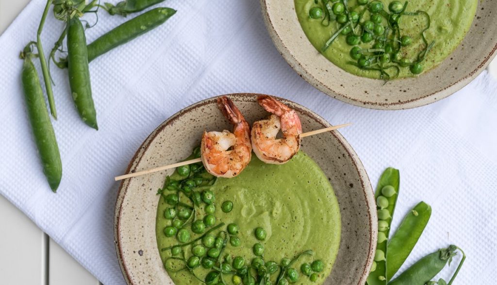 Grüne Erbsensuppe mit Garnelenspieß in einer grauen Schale 