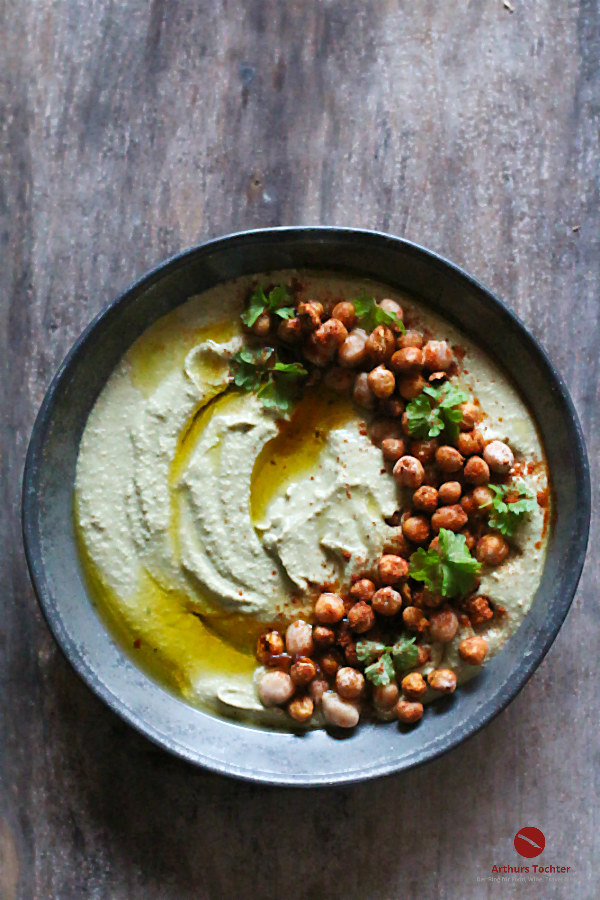 Hummus mit gerösteten Kichererbsen und Olivenöl in einer grauen Schale 