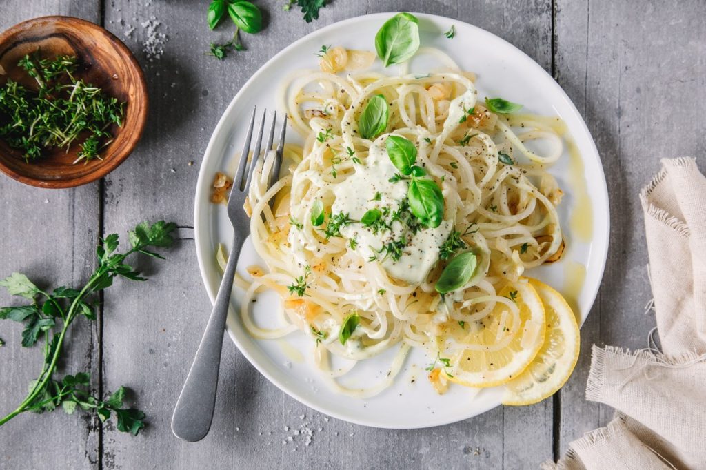 Kohlrabi Spaghetti mit heller Soße und Basilikum auf einem weißen Teller