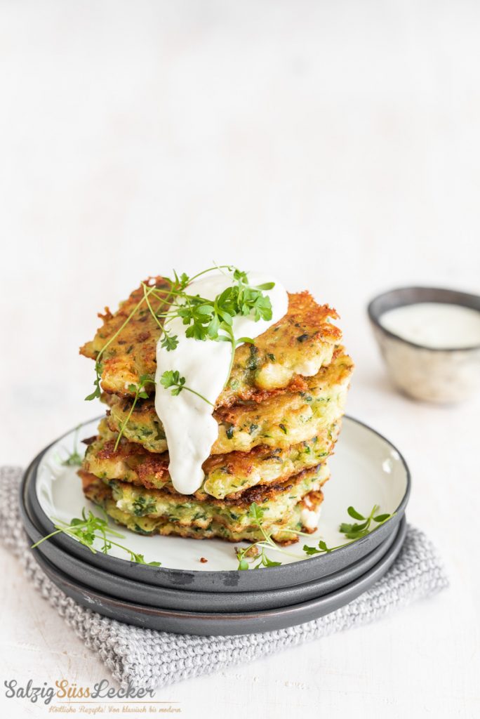 Zucchini Bratlinge aufgeschichtet, darauf ein Joghurtdipp und Kräuter
