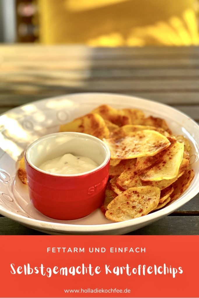 Selbstgemachte fettarme Kartoffelchips auf einem hellen Teller, mit einem Dip im roten Schälchen daneben. Vorlage für Pinterest.