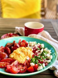 Auf einem türkisen Teller sind Rühreier, Tomaten und Schafskäse 