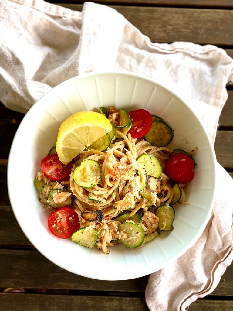 Ein Teller Pulled Lachs Pasta von oben fotografiert, mit Tomaten und Zitrone 