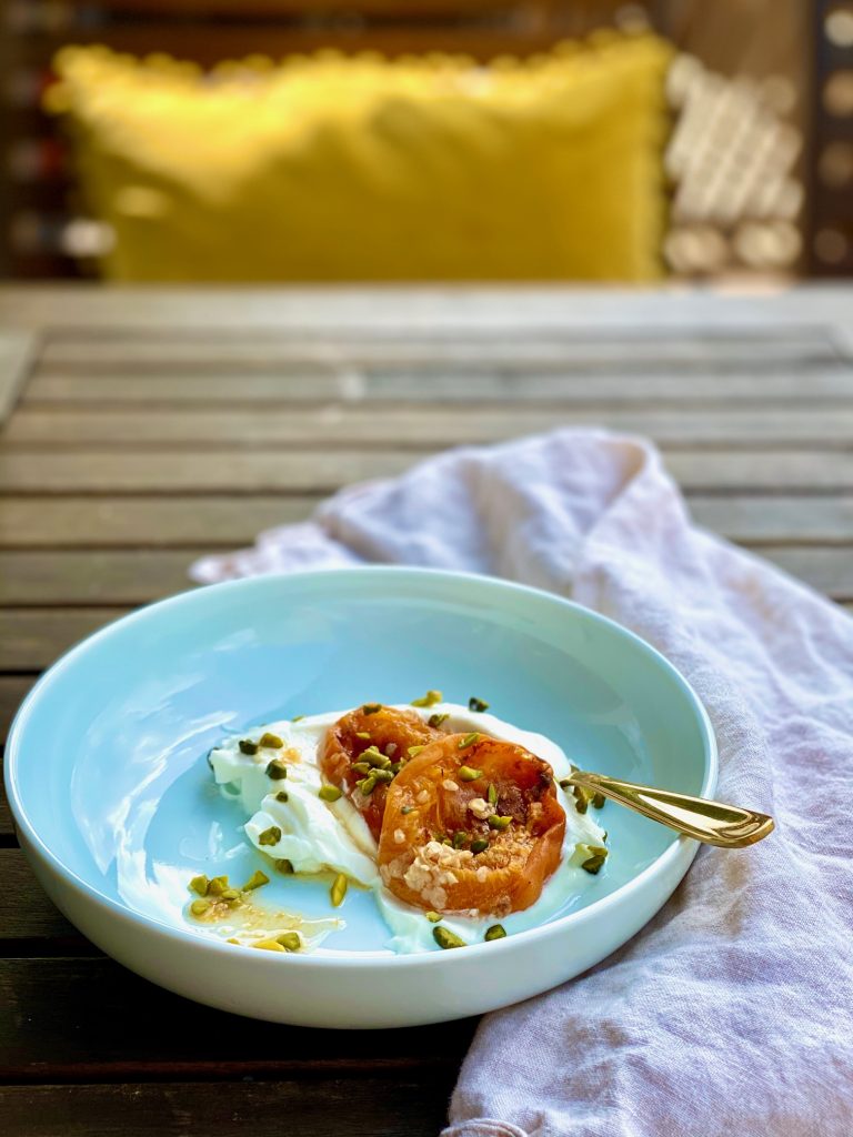 Blaue Schale mit Quark, darauf gratinierte Aprikosen mit Pistazien und einem goldenen Löffel