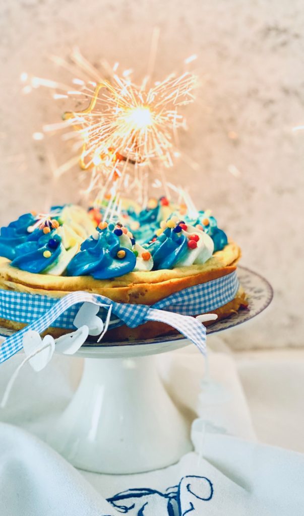 Cheesecake mit blauem Tapping und Zuckerperlen mit einer angezündeten Stern-Wunderkerze 