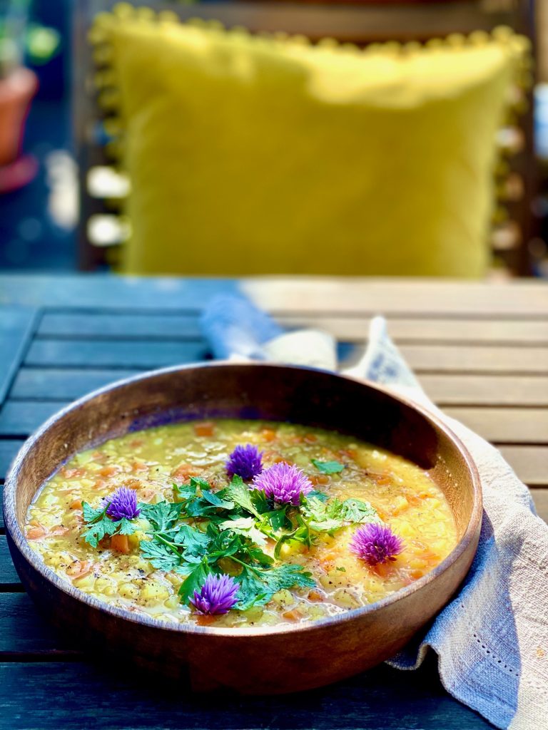 Schnelle bunte Linsensuppe mit Gemüse, auf einem Holzteller draussen fotografiert 