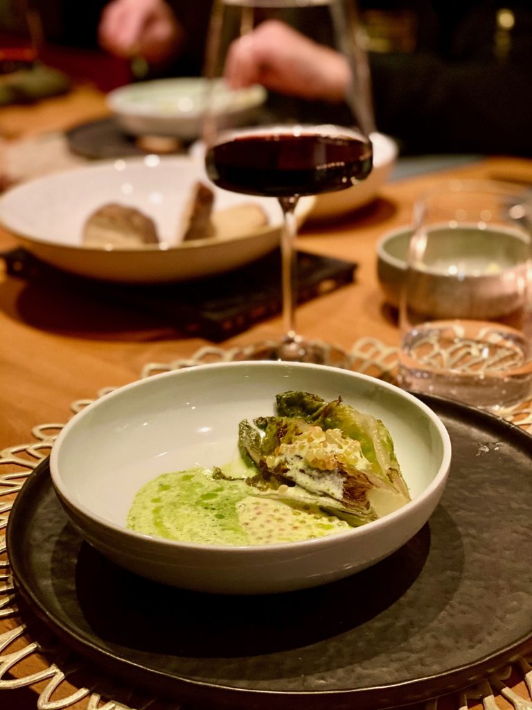 Veles Restaurant Nürnberg kurzgebratenes Salatherz mit einer Vinaigrette aus Saiblings-Rogen, Joghurt und Dill mit Rotwein im Hintergrund