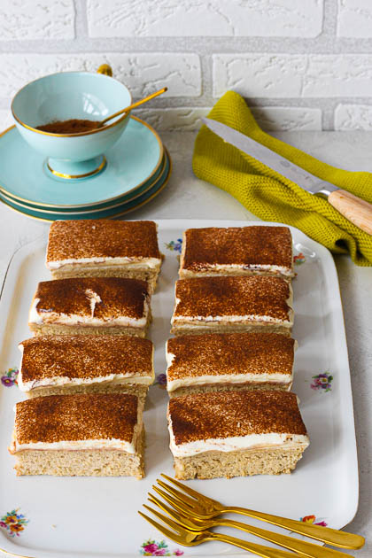 Bananenkuchen mit Skyr-Frosting und Zimt, dahinter eine Blaue Tasse mit Zimt 