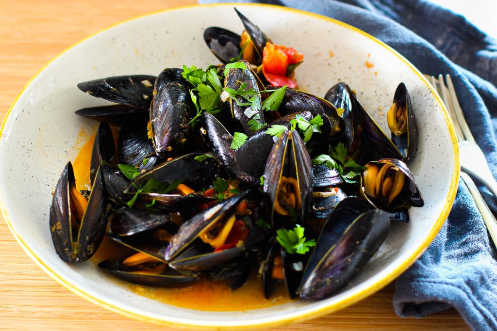 Miesmuscheln in Tomaten-Weißweinsoße auf einem Steingut Teller 