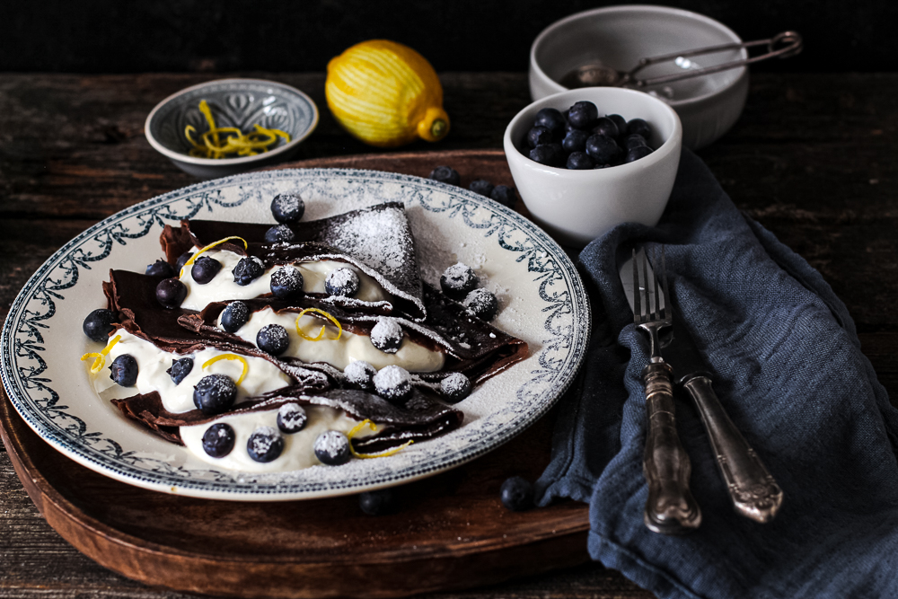Schoko Crêpes mit Blaubeeren auf einem alten bemalten Teller