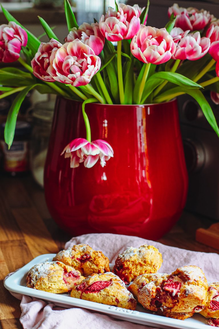 Einfache Scones mit Erdbeeren und Dinkelmehl auf einer weißen Platte vor pinken Tulpen