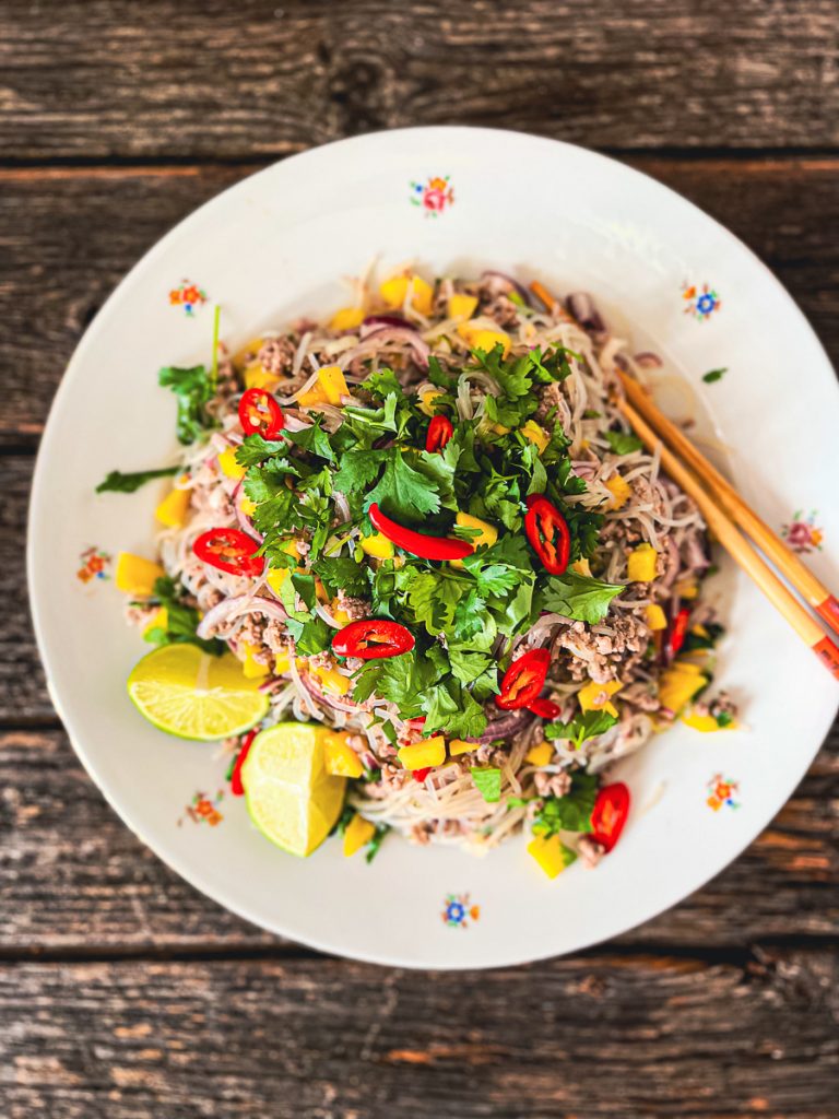 Einfacher Glasnudelsalat mit Rindfleisch und Mango von oben fotografiert, auf einem alten Teller mit Blumen