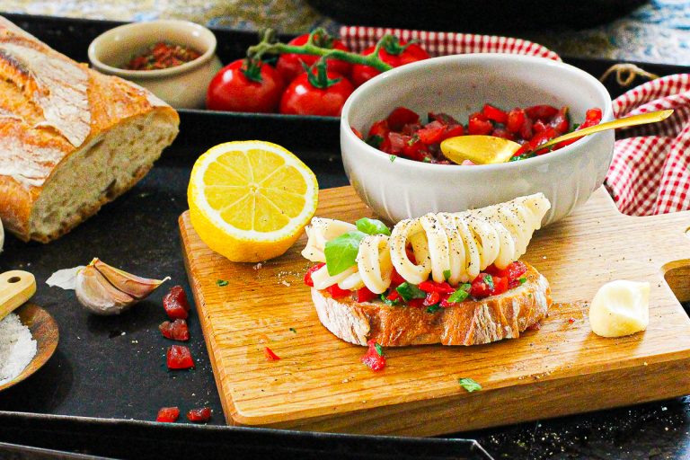 Knusprige Crostini mit Tomaten und Tintenfisch, Nahaufnahme von einem Crostini auf einem Brett
